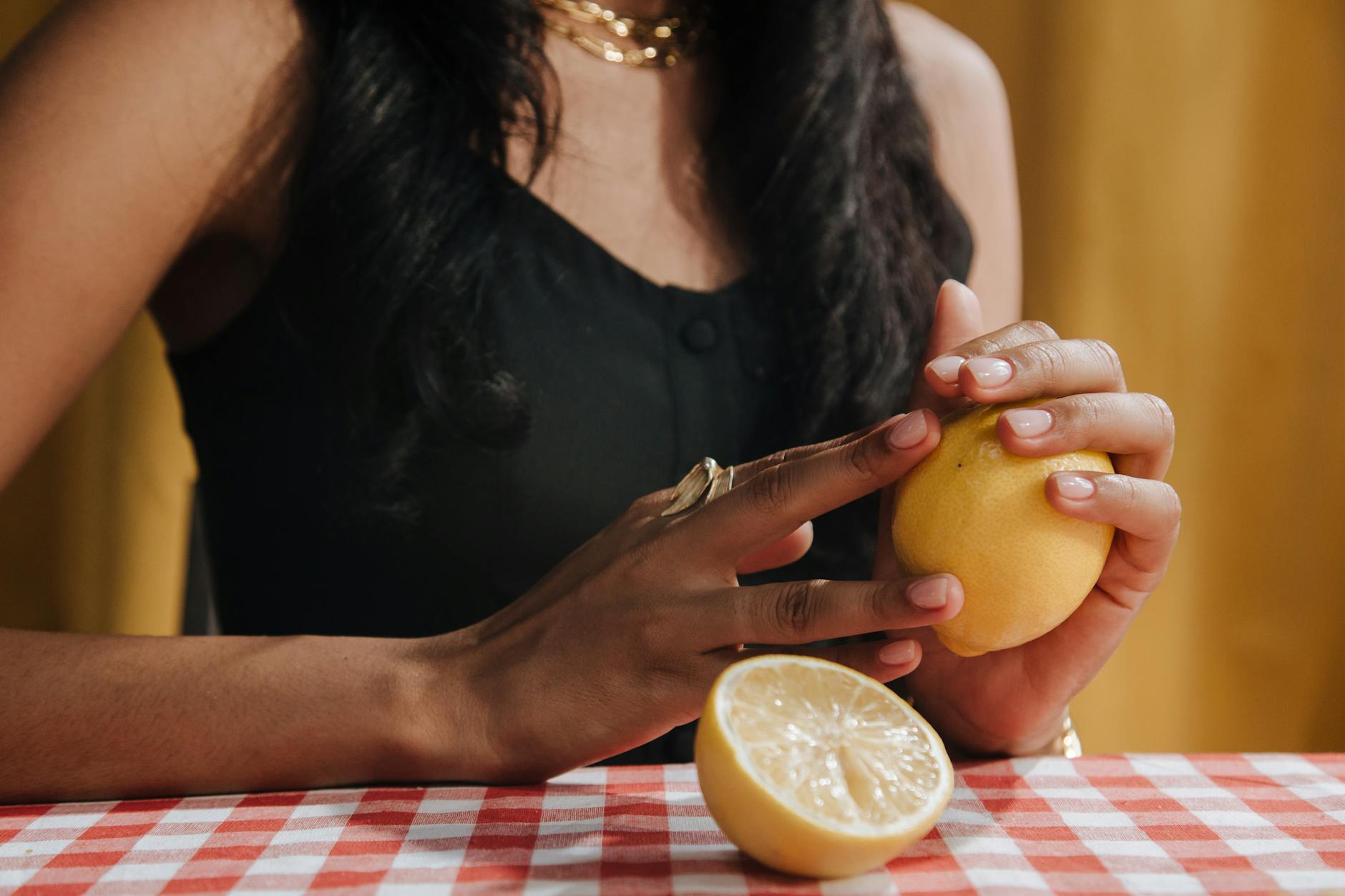 Close-up of a woman with dark hair holding a fresh lemon at a dining table, symbolizing renewed connection to sensation