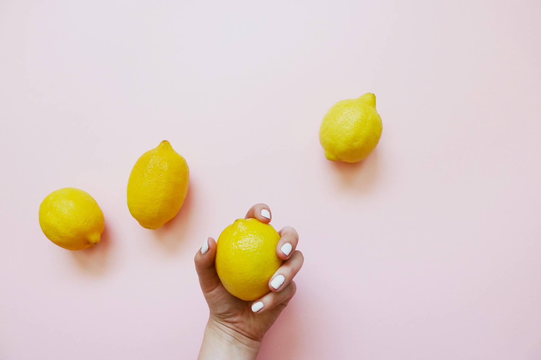 A hand holding a bright yellow lemon on a soft pink background, symbolizing fresh approaches to desire