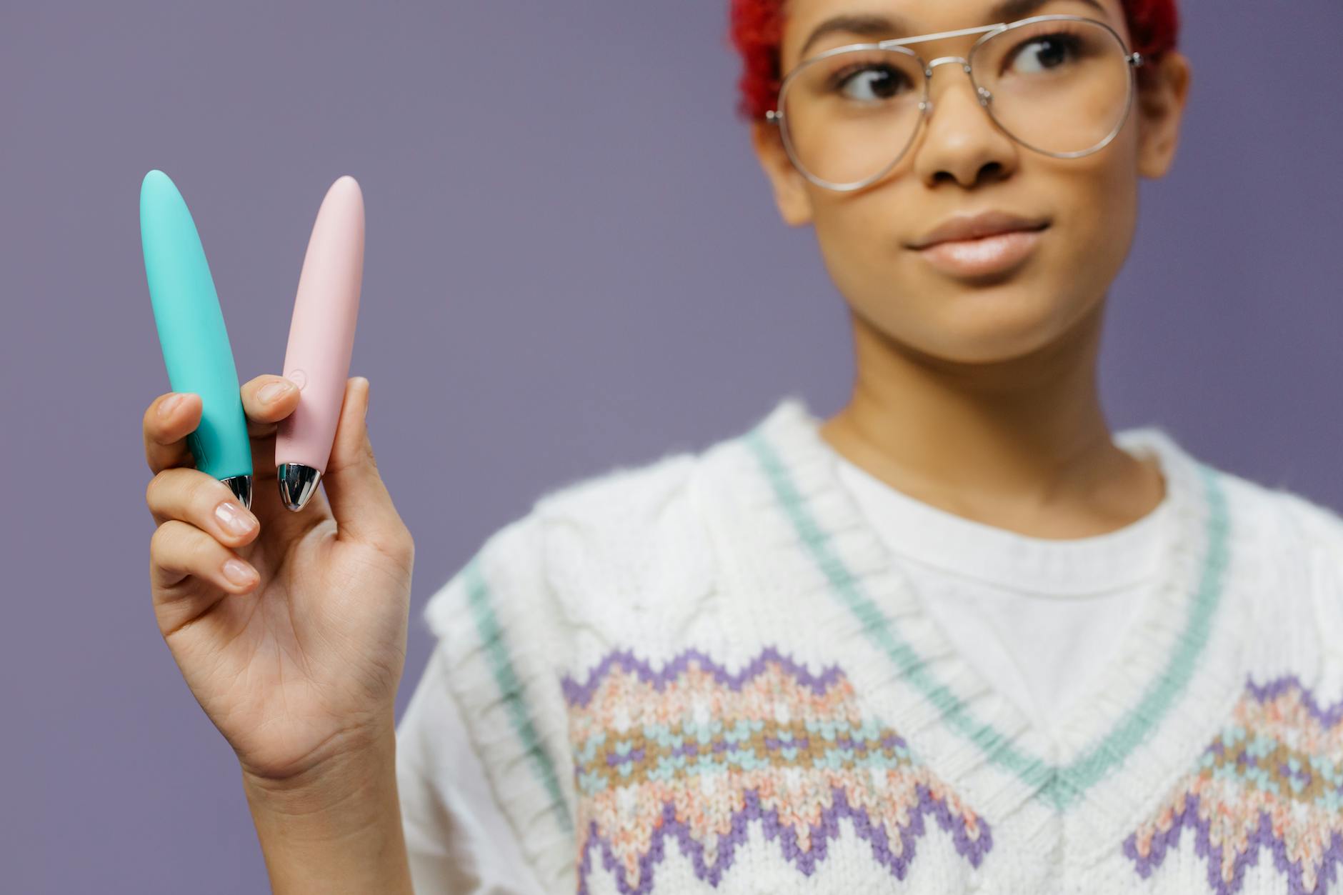 Person holding vibrators against colorful background, representing tools for sexual wellness