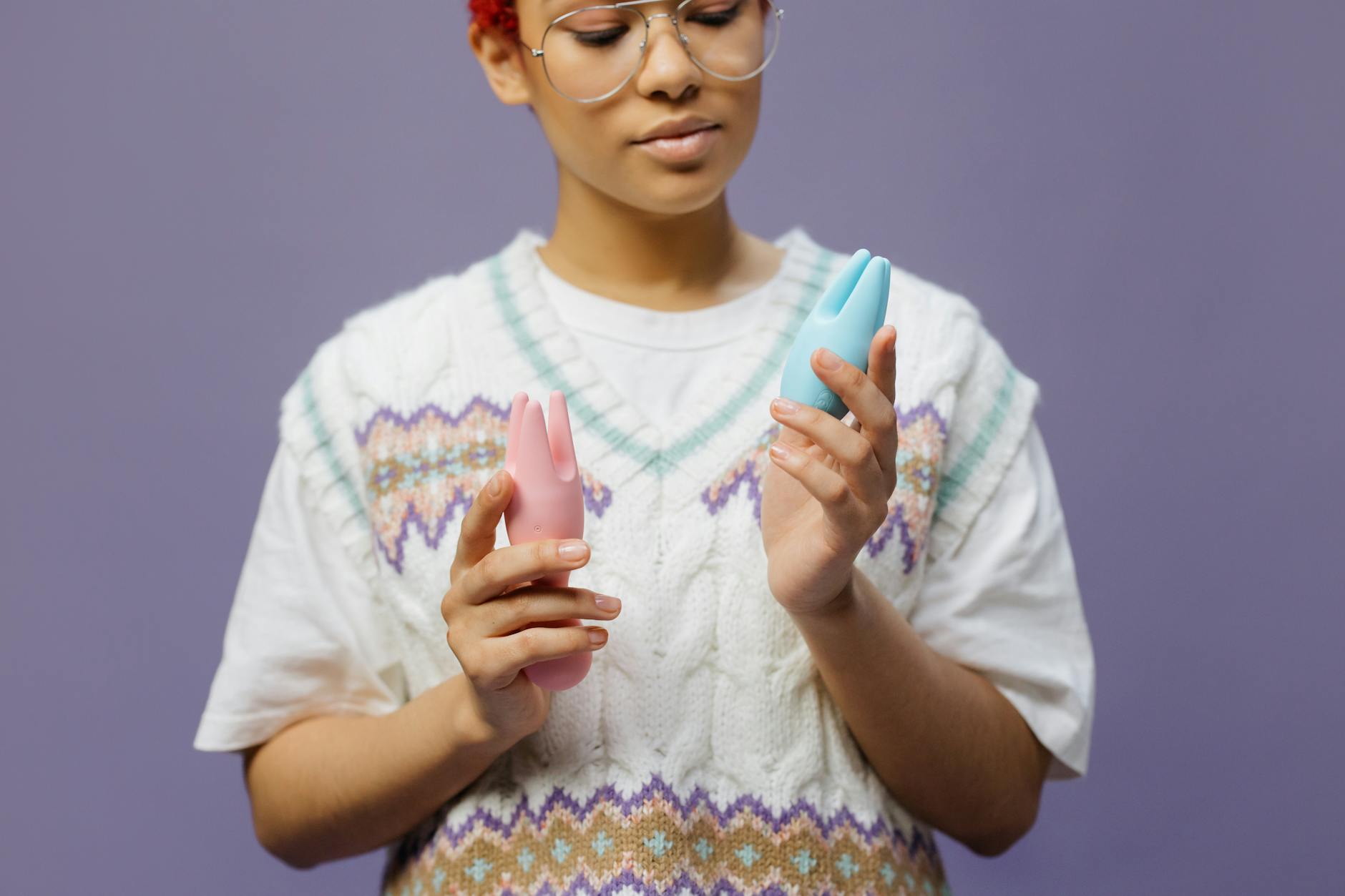A person holds an orange vibrator against a minimalistic purple backdrop, showcasing modern sensuality and self-care.