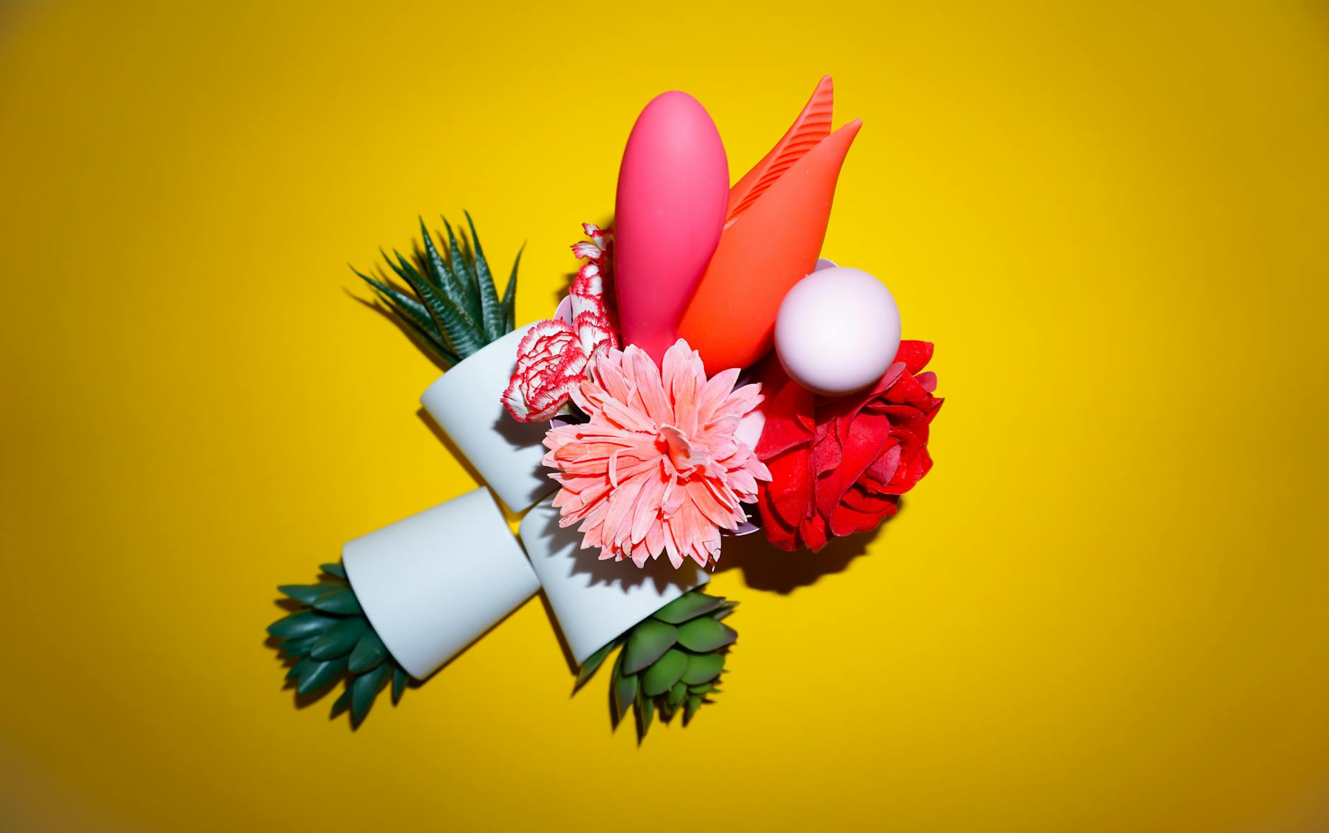 Colorful arrangement of flowers and vibrator on bright yellow background, representing pleasure and self-discovery